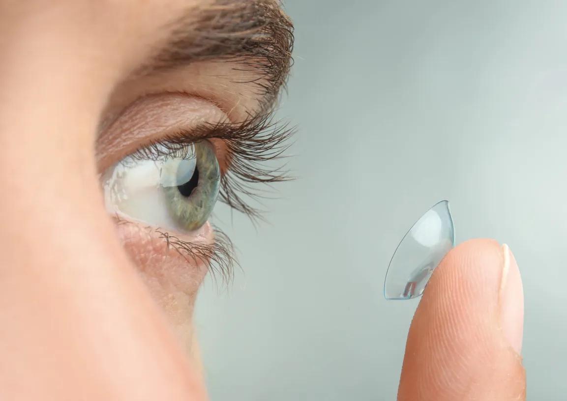 Foto zeigt eine Nahaufnahme eines Auges und einen Finger auf dem eine Kontaktlinse liegt